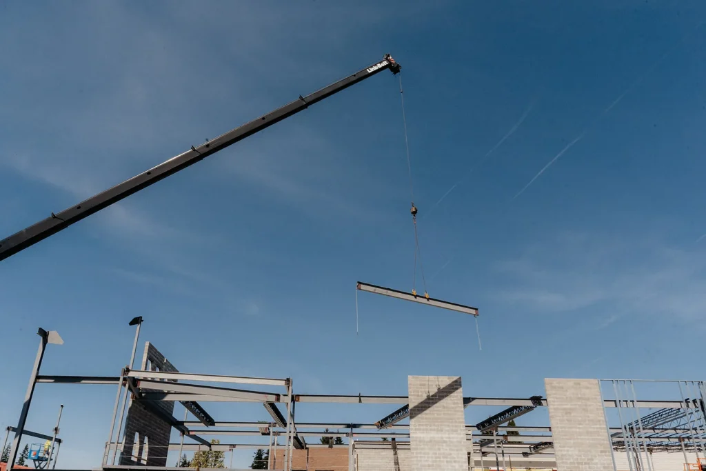 Westmore crane boom and rigging lifting a steel beam over a frame against a blue sky