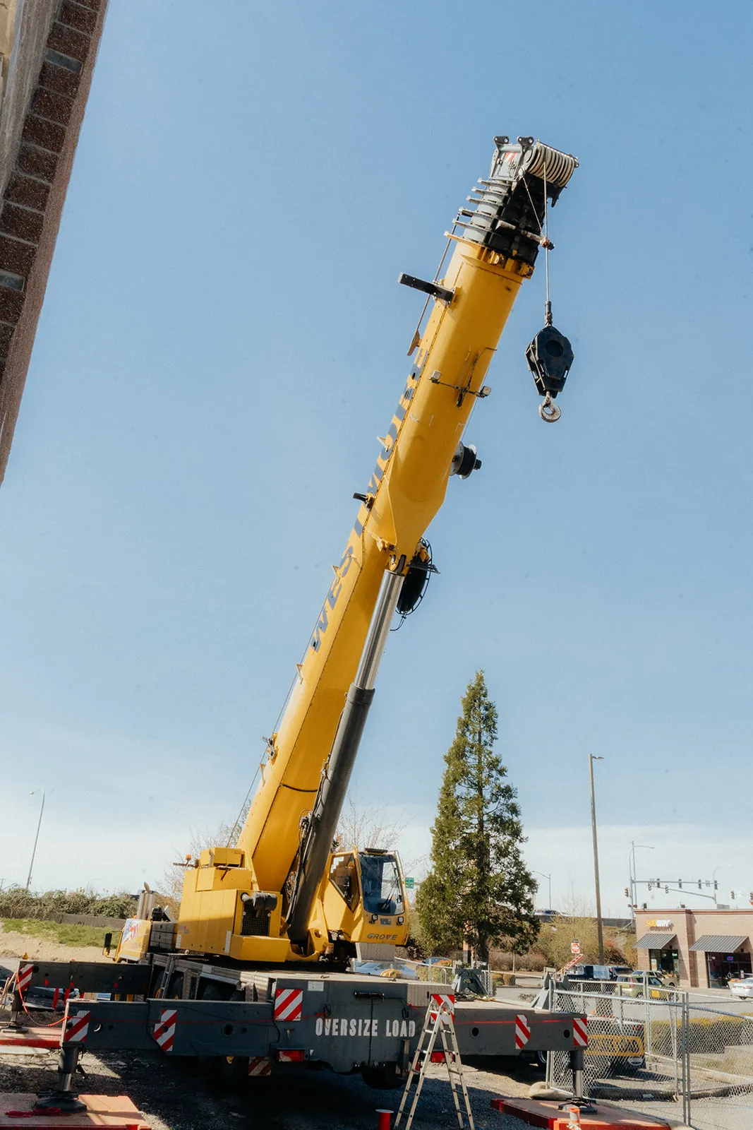 Yellow Grove crane with the boom raised beside a brick building