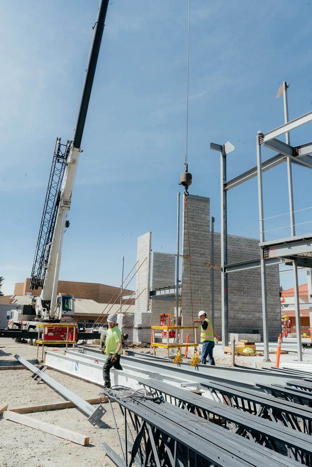 Crane lifting a steel beam over a partially erected commercial frame